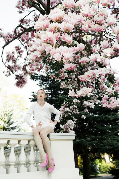 Free photo pretty girl is sitting at the railing under the amazing magnolia tree