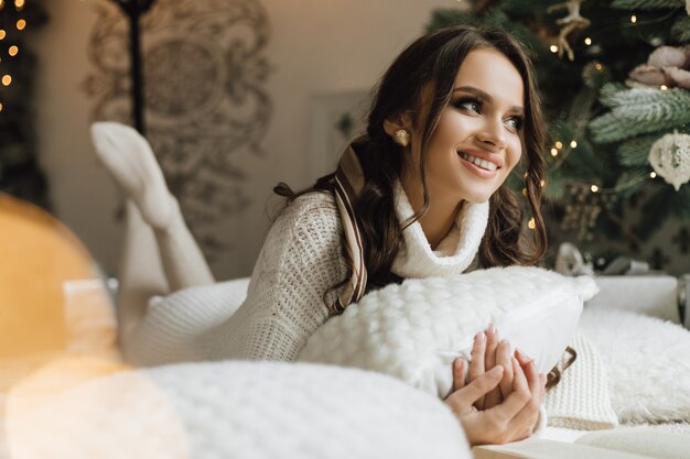 Pretty girl lies with pillows near a Christmas tree