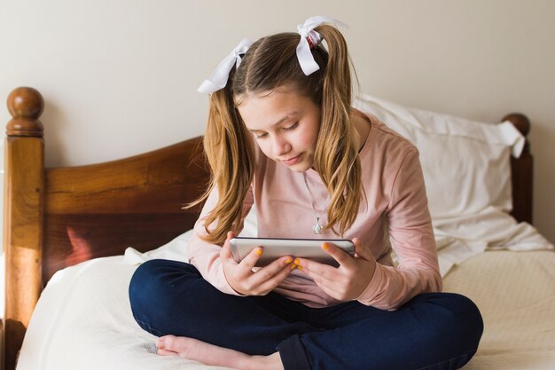 Pretty girl sitting on bed looking at smartphone