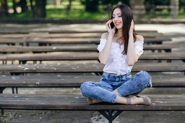 Pretty girl talking on the phone sitting on the bench in a park