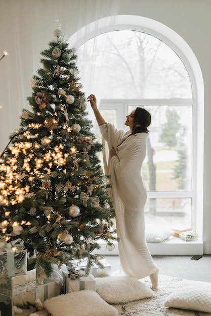 Pretty girl wrapped in a plaid is hanging a toy on a Christmas tree