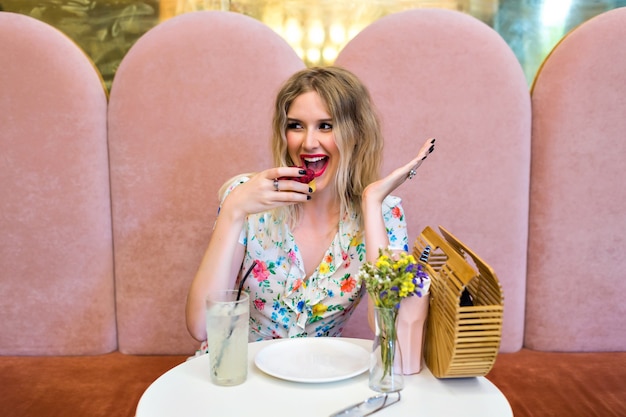 Free Photo pretty happy blonde hipster woman eating  tasty raspberry dessert cake, sitting at cute bakery, enjoy her meal, sweet breakfast, diet nutrition concept.