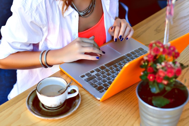 Free photo pretty hipster girl working on her laptop at city cafe, coworking place, young freelancer tap on notebook, summer atmosphere.