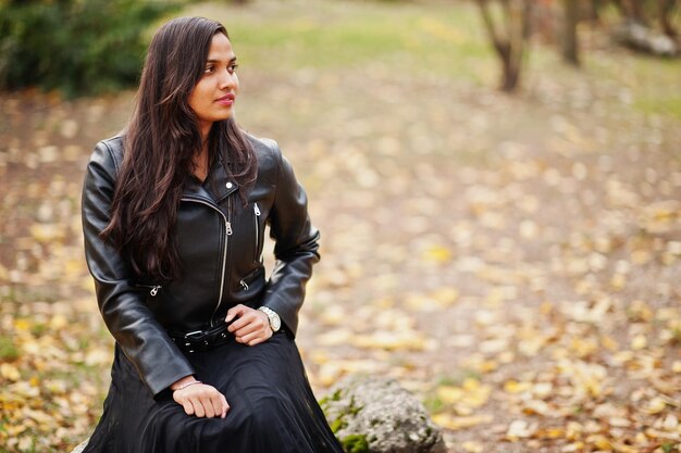 Pretty indian girl in black saree dress and leather jacket posed outdoor at autumn street