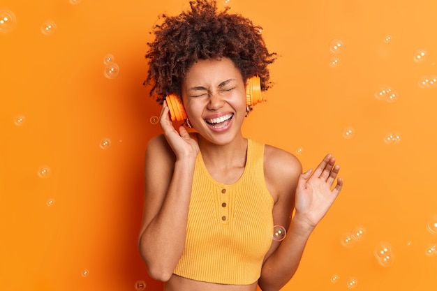 Free Photo pretty joyful dark skinned teenage girl listens music via headphones closes eyes and smiles broadly