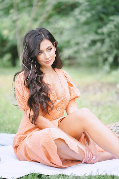 Free photo pretty lady in orange dress sitting and looking far in nature during daytime .