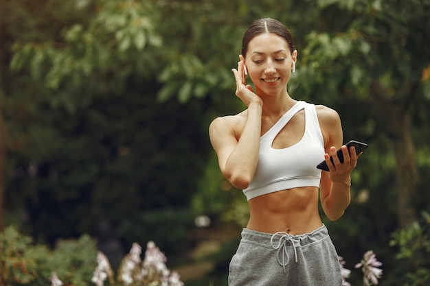 Pretty lady in a park. Brunette with mobile phone. Girl in a sportsuit.