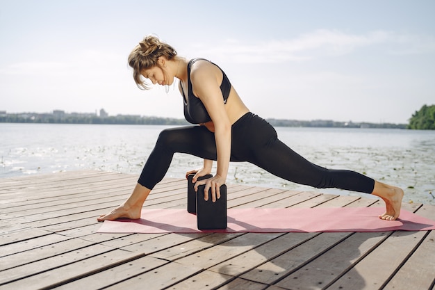 Pretty lady training in a summer park. Brunette doing yoga. Girl in a sportsuit.