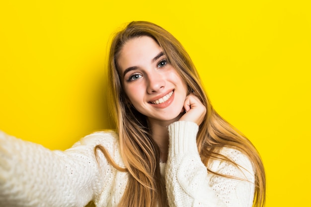 Free photo pretty lovely smiling fashioned girl is making selfie on her phone wearing wide white sweater on yellow