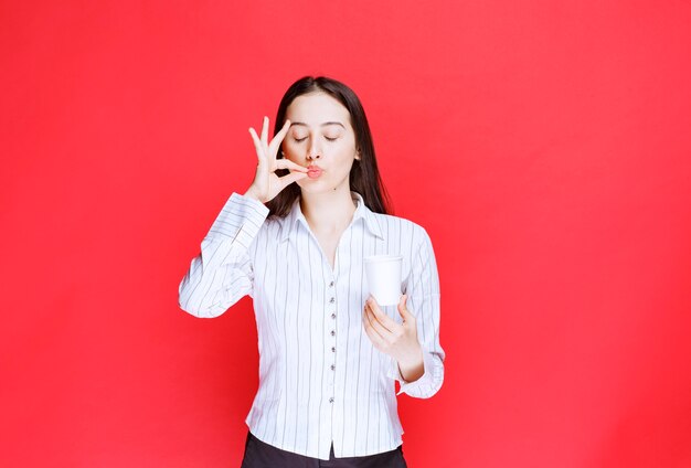 Pretty office employee posing with plastic cup of tea over red wall. 