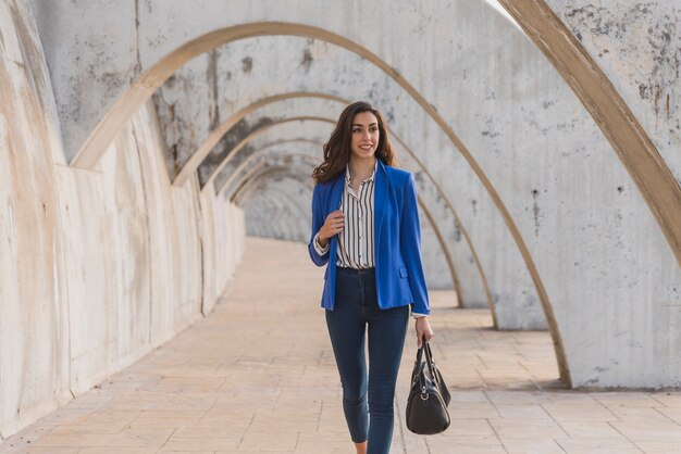 Pretty smiling girl holding her handbag and walking