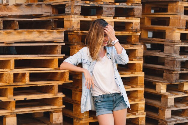 Pretty smiling girl, wearing jeans, shorts and shirt posing on wood background