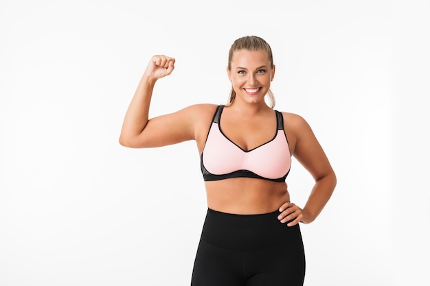 Pretty smiling plump girl in sporty top and leggings happily looking in camera over white background isolated