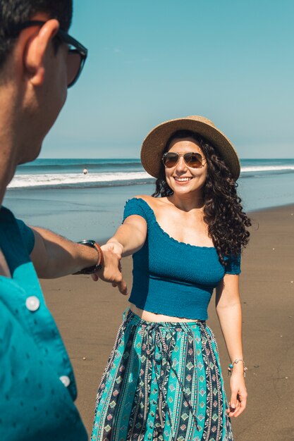 Pretty smiling woman pulling man to beach 