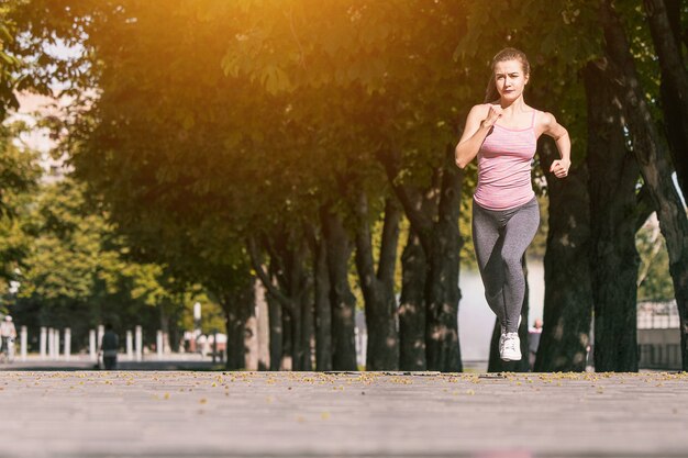 Pretty sporty woman jogging at park in sunrise light