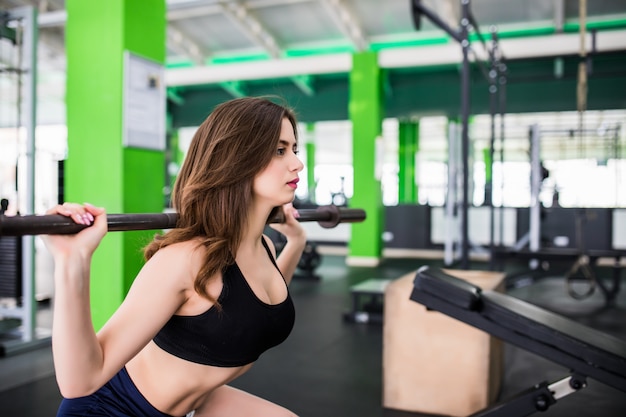 Pretty strong young woman doing exercises squatting with barbell dressed up in fashion sportswear in sportclub