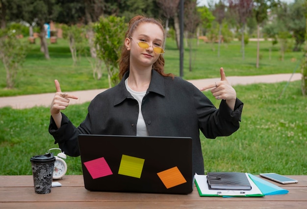 Pretty student freelancer programmer working at laptop looking at camera