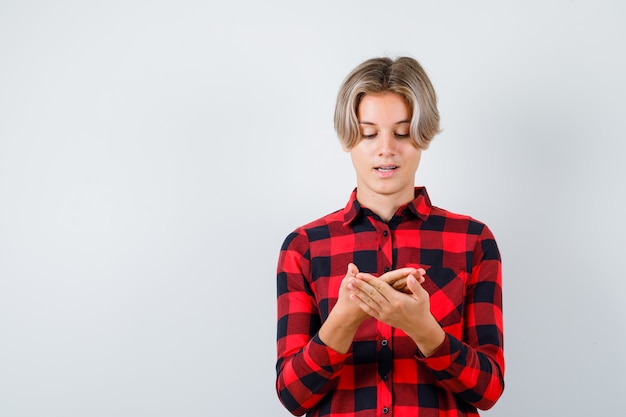 Pretty teen boy looking at his palm in checked shirt and looking hopeful , front view.