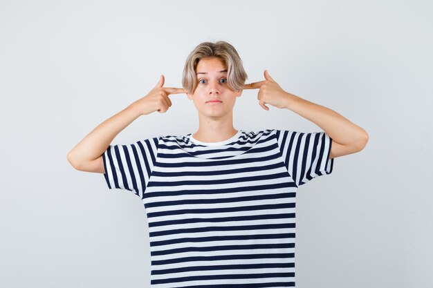 Pretty teen boy plugging ears with fingers in striped t-shirt and looking bewildered , front view.