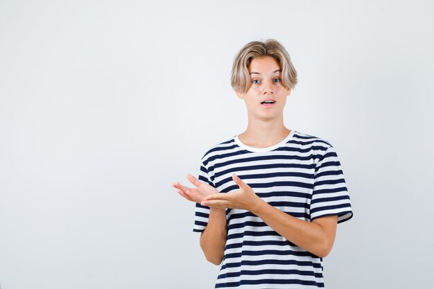 Pretty teen boy in striped t-shirt pretending to show something and looking puzzled , front view.