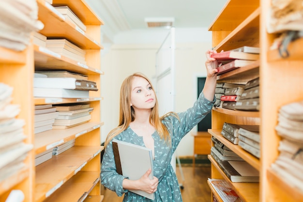 Free Photo pretty teenager taking textbooks from shelf