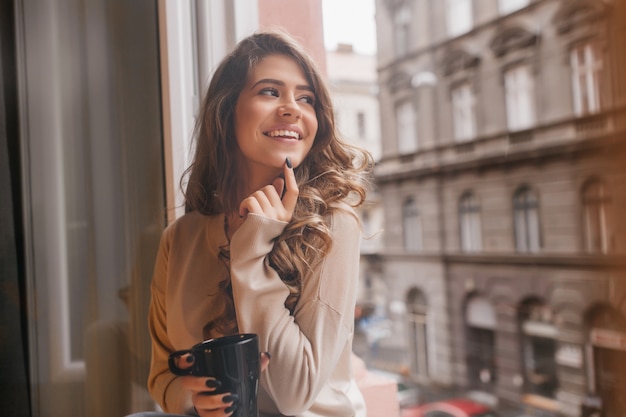 Pretty white woman playfully touching chin with finger while looking at city