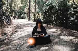 Free photo pretty witch reading old tome in woods on road