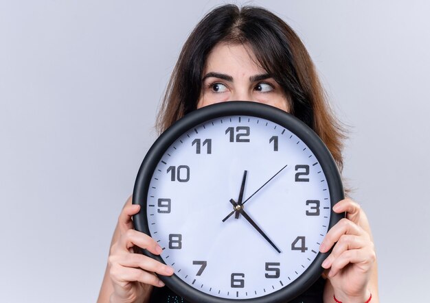 Pretty woman in black blouse hiding behind the clock looking besides 