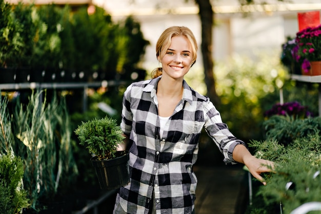 Pretty woman in cute clothes reaching for plants in greenhouse