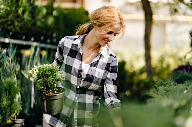 Pretty woman in cute clothes reaching for plants in greenhouse