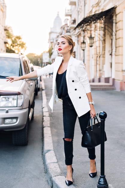 Free photo pretty woman on heels catching a taxi in city. she holds a bag in hand.