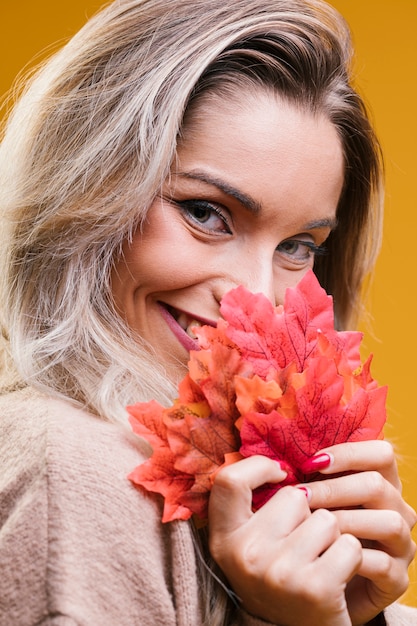 Pretty woman holding maple leaves looking at camera