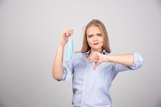 Free photo pretty woman holding mask and giving thumbs down