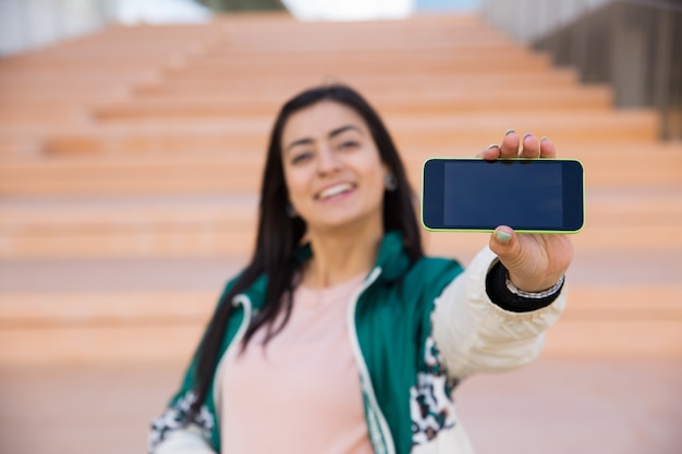 Pretty woman making selfie on phone, smiling. Gadget on focus