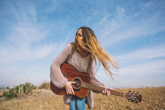 Free photo pretty woman playing guitar in field