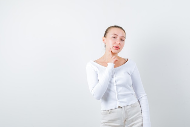 Pretty woman puts her finger on her cheek on white background