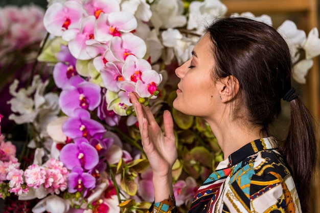 Pretty woman smelling pink flowers in green house