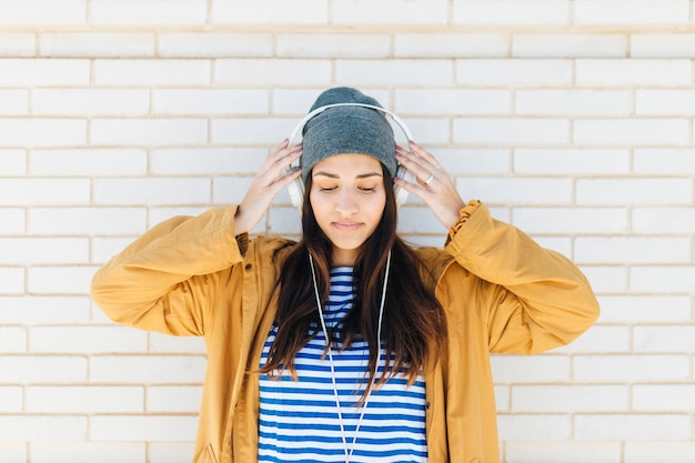 Free photo pretty woman standing against white brick wall wearing headphones