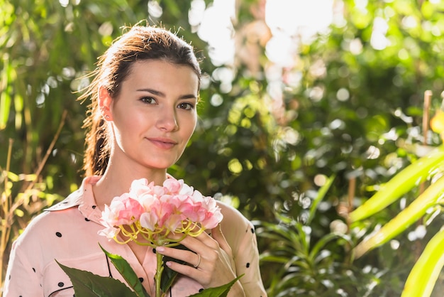 Free photo pretty woman standing with pink flower in hand