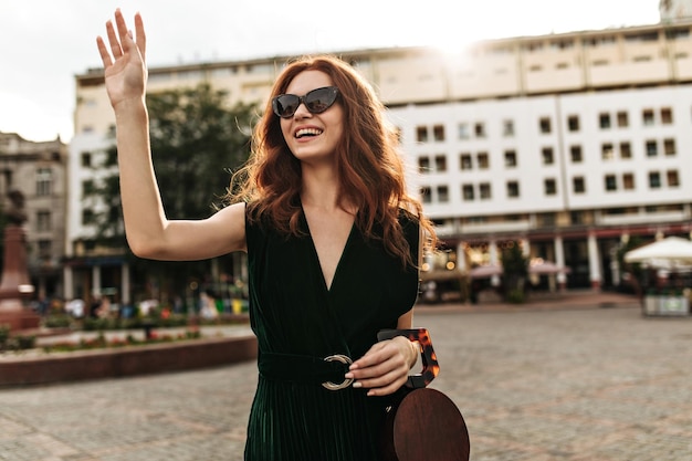 Free photo pretty woman in velvet dress holds handbag and waving hand