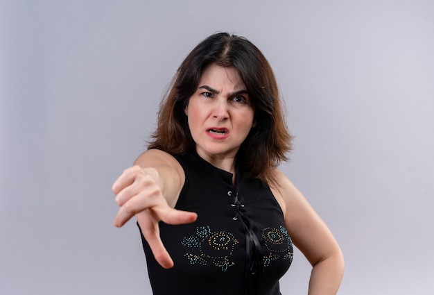 Pretty woman wearing black blouse angrily jawing with forefinger over gray background