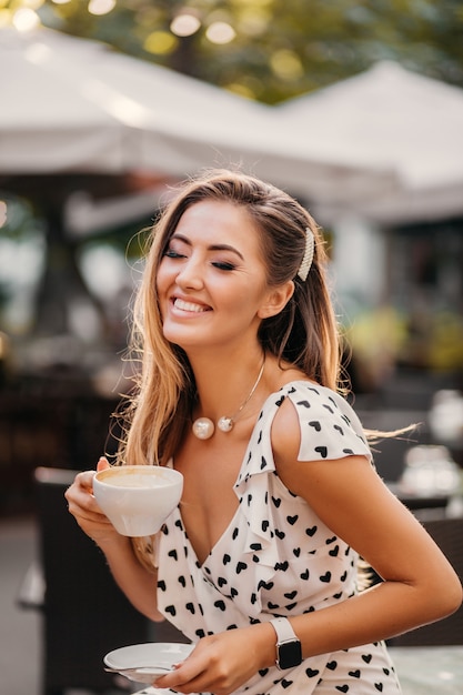 Free photo pretty woman with candid smile laughing sitting at summer cafe with a cup of cappuccino