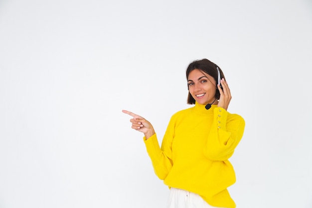 Pretty woman in yellow sweater on white  manager with headphones happy smile point finger left