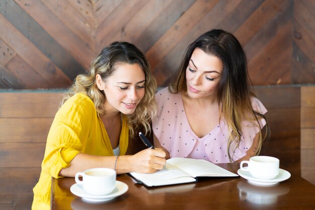 Pretty women drinking coffee and writing in notebook in cafe