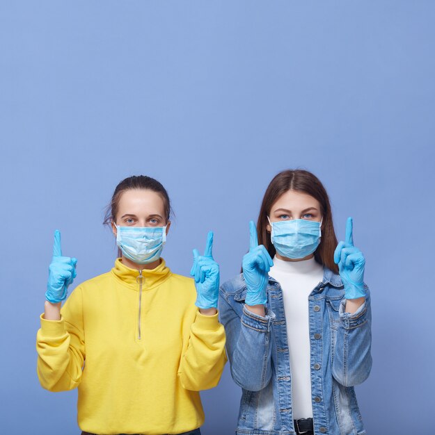 Pretty women wearing medical masks and latex gloves pointing index fingers