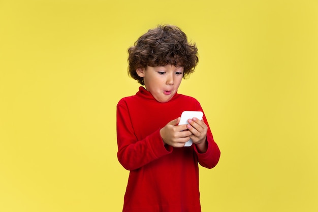 Pretty young curly boy in red wear on yellow wall childhood expression fun