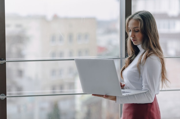 Pretty young girl with laptop by the window