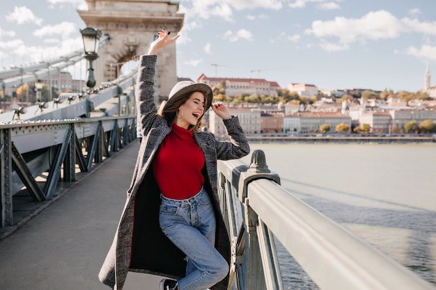 Free photo pretty young woman in blue jeans and long coat dancing on bridge near triumphal arch