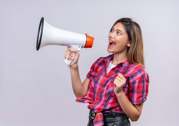 A pretty young woman in checked shirt speaking through megaphone on a white wall