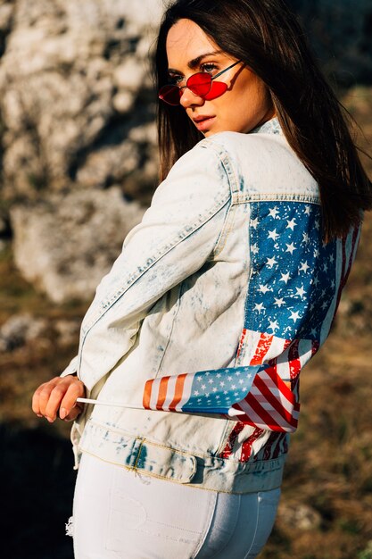 Pretty young woman in denim jacket with American flag on sunny day